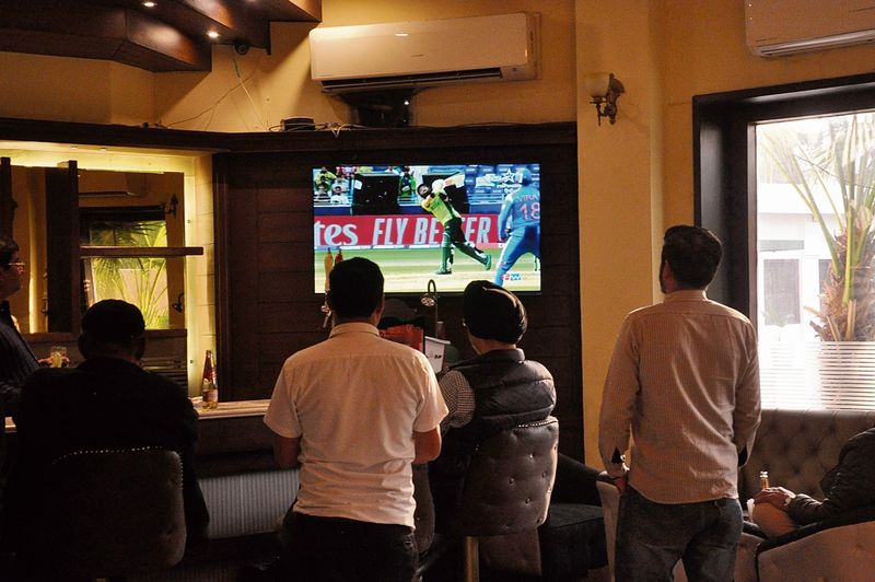 Image: Families and friends gathered around television screens watching an India-Pakistan cricket match